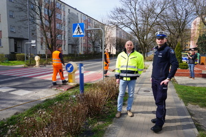 Na zdjęciu policjant, służby komunalne oraz naczelnik wydziału dróg podczas otwarcia nowej kampanii i malowania napisów przed przejściem dla pieszych.